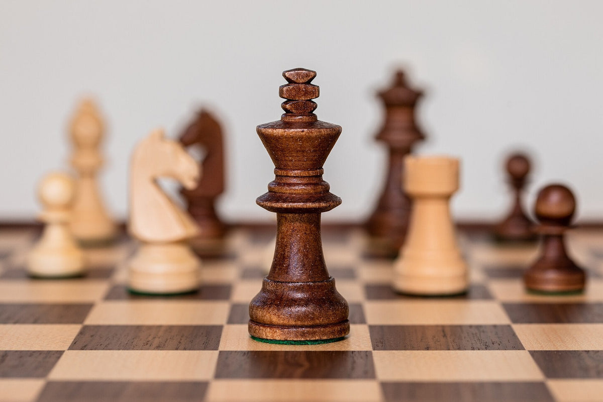 Staunton king standing among wooden chess pieces