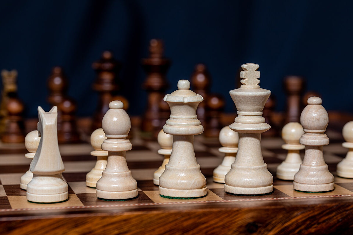 Light wooden chess pieces on a walnut board against a dark background